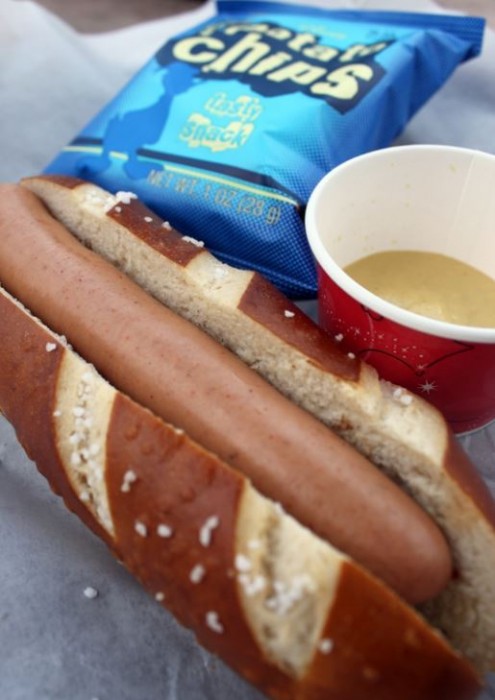 Frankfurter in a pretzel roll served with chips and Dijon mustard